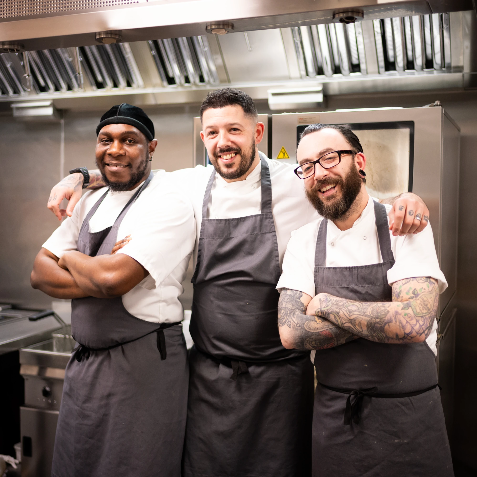 Three smiling chefs with aprons in a kitchen.