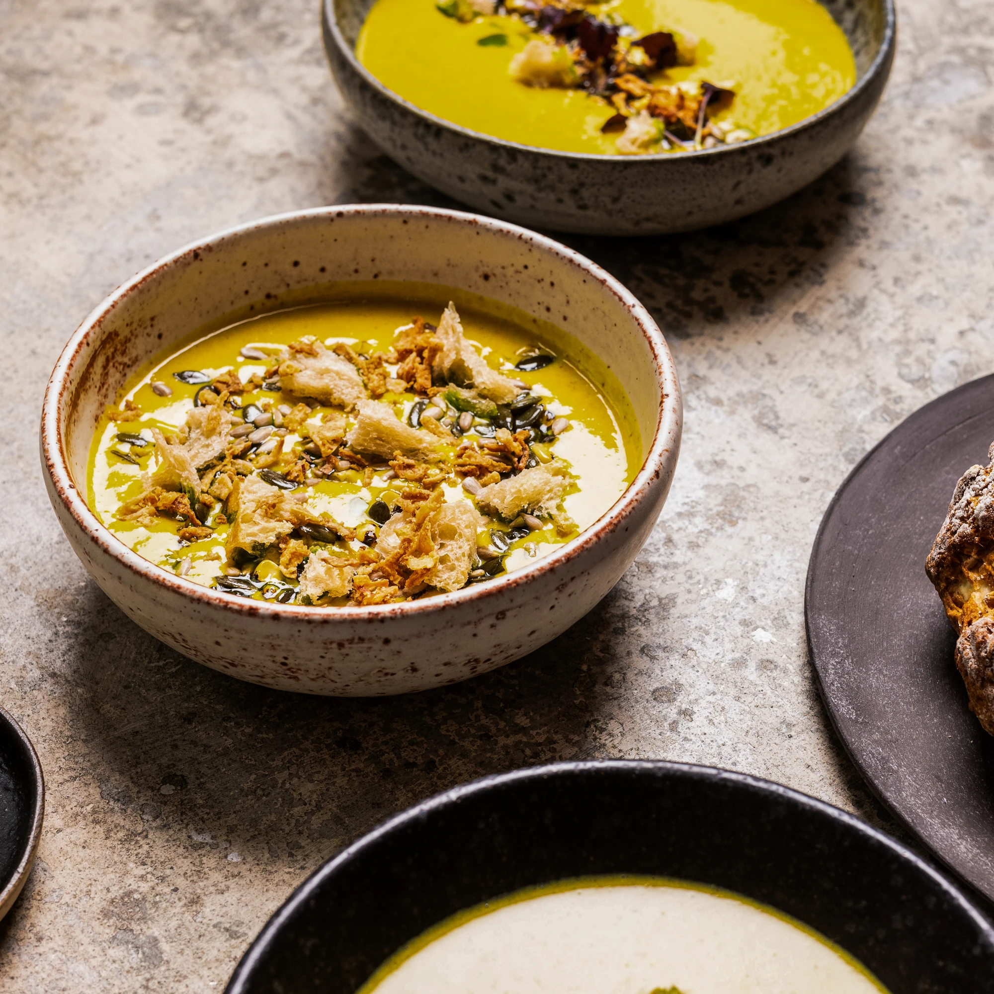 Three bowls of creamy soup topped with croutons and seeds.