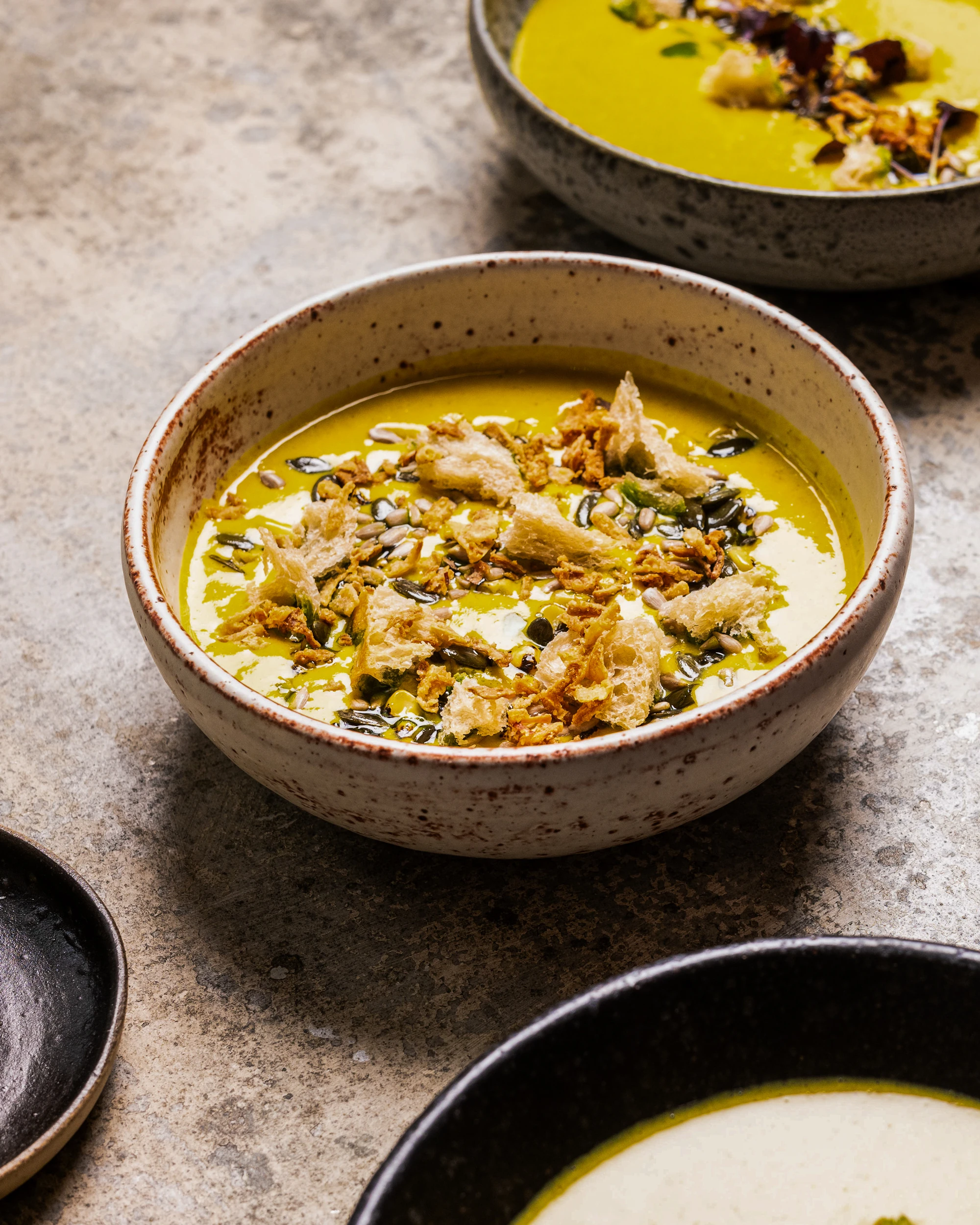 Three bowls of creamy soup topped with croutons and seeds.