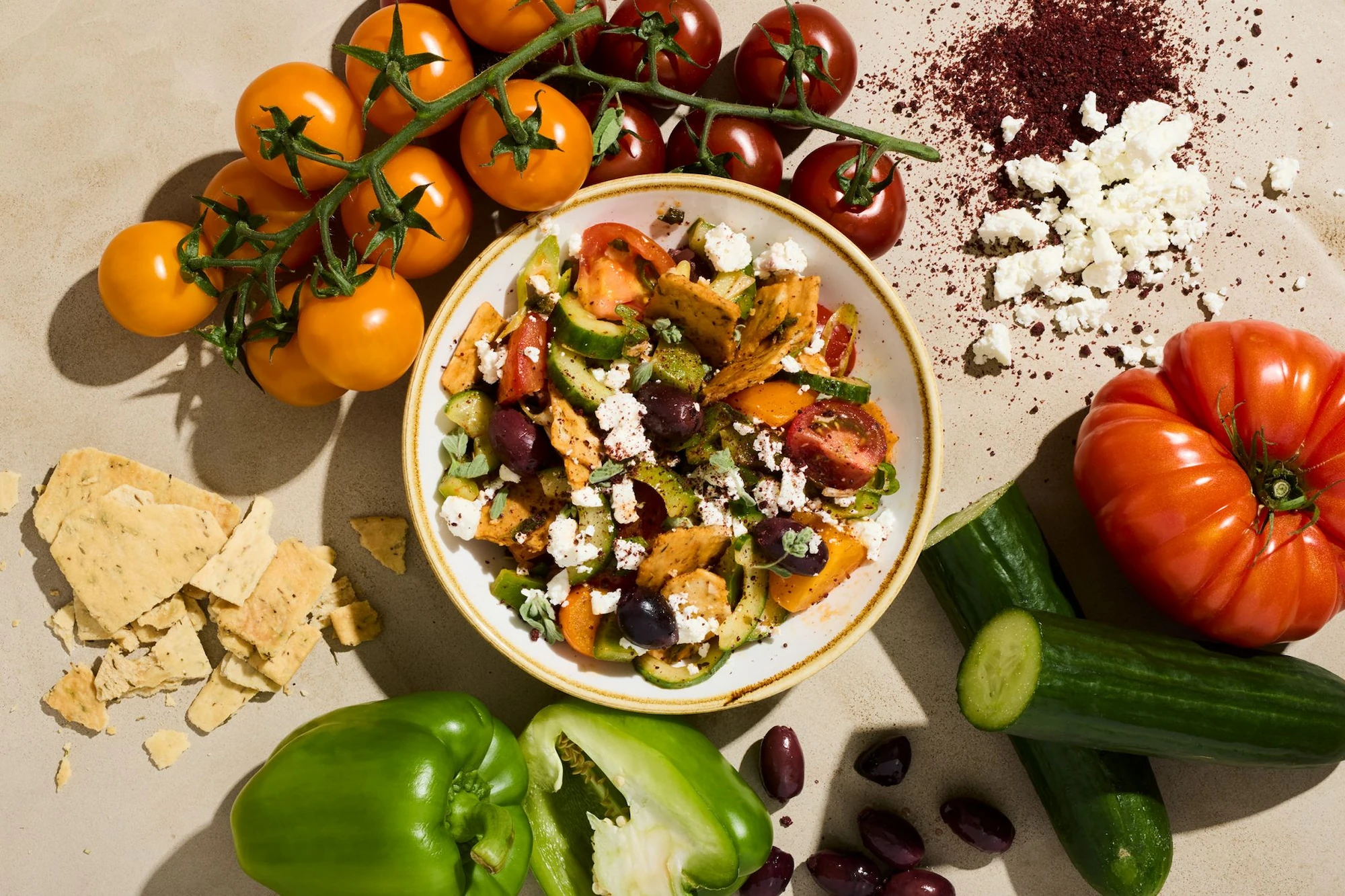 Overhead view of a colourful salad surrounded by fresh vegetables.